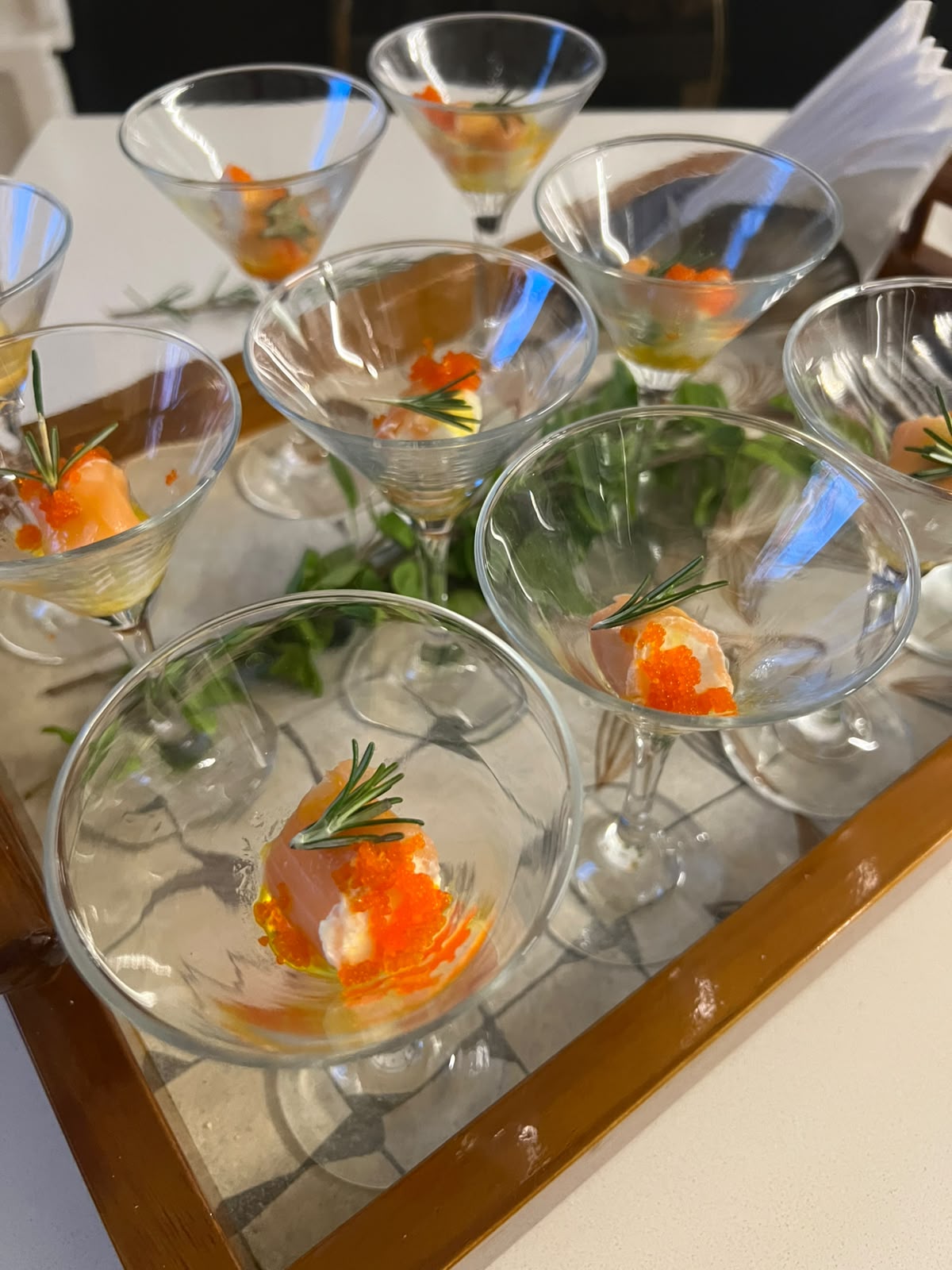 taças de martini com entrada de salmão e ovas de peixe decoradas com alecrim sobre bandeja de espelho