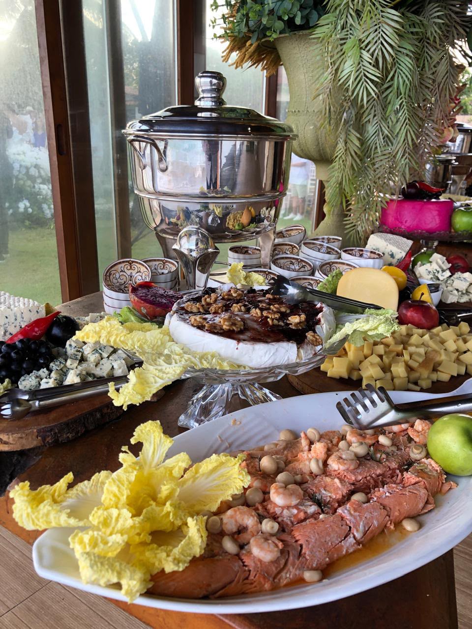mesa de buffet com salmão ao molho com camarões no primeiro plano, brie com geleia e nozes, queijos variados e